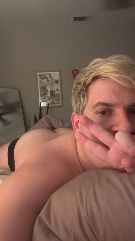 Man laying on bed holding a peace sign with his butt visible