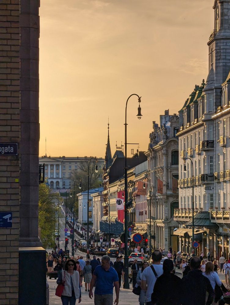 View of a long street in Oslo during sunset with people walking on the sides.