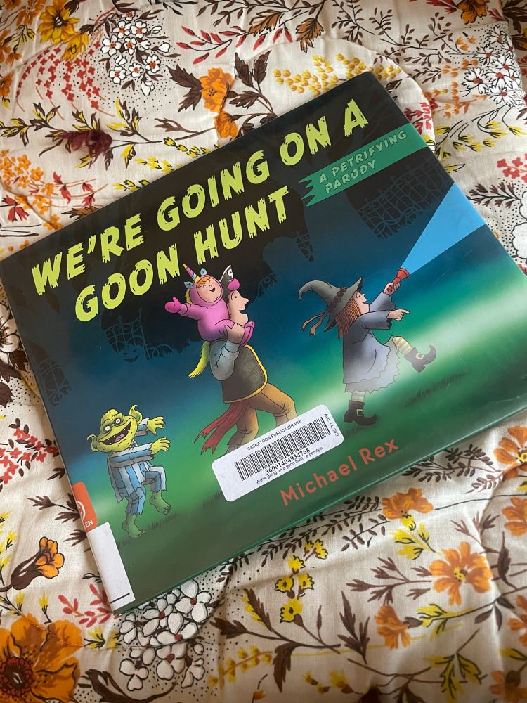 A hardcover copy of We’re Going on a Goon Hunt laying on a vintage floral blanket 