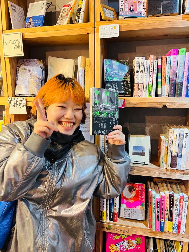 笑顔でピースサインをしている高島鈴さん。手に著書『布団の中から蜂起せよ』を持っている。