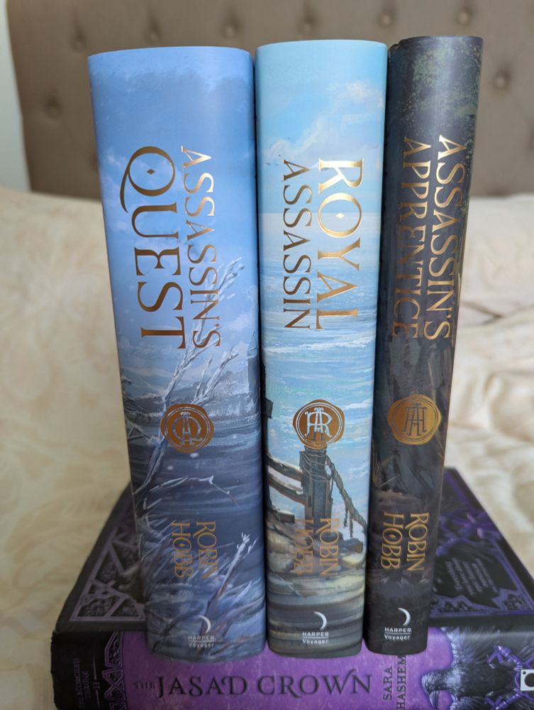 Trilogie de l'assassin royal en édition spéciale, jolies jaquettes et travail sur les tranches représentant une ville médiévale sur une falaise en nuances de gris et de bleus 