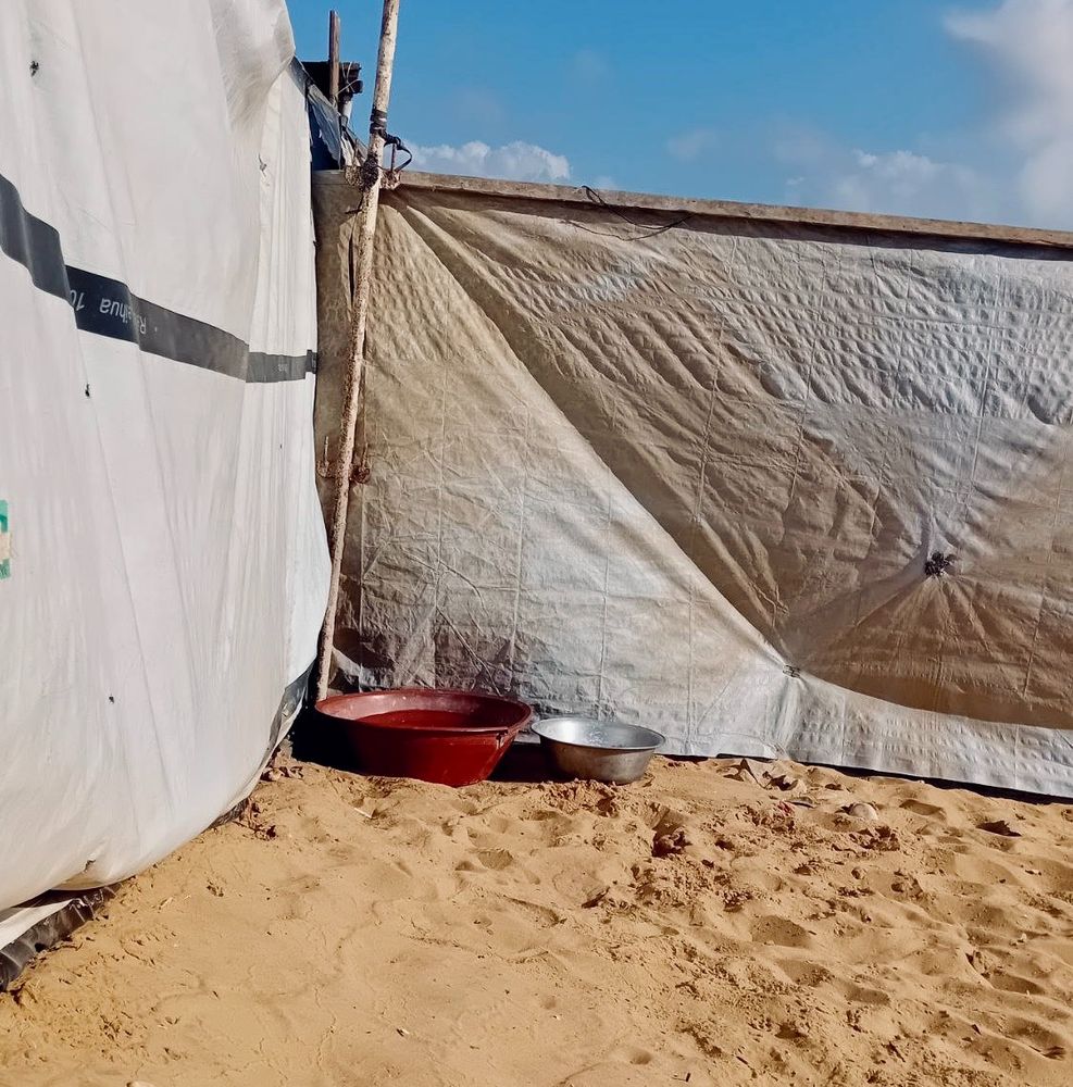 a corner of the smoothed-over sandy area, with a couple of wide, low bowls in the corner between two cloth/treated cloth (?) "walls" held up with poles.