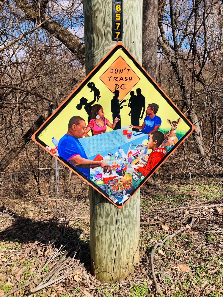 A beautiful street pole sign by a local Ward 8 artist featuring neighbors communing with wildlife and saying - Don’t Trash DC. 