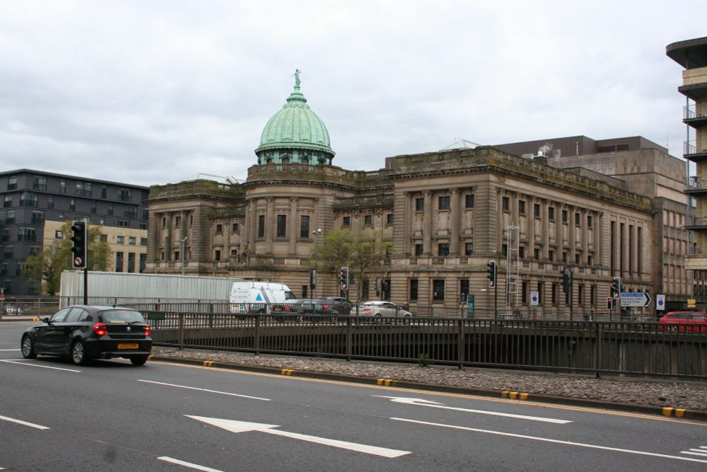 View of Mitchell Library in Glasgow, featuring its prominent green dome, captured from across the street with passing vehicles.