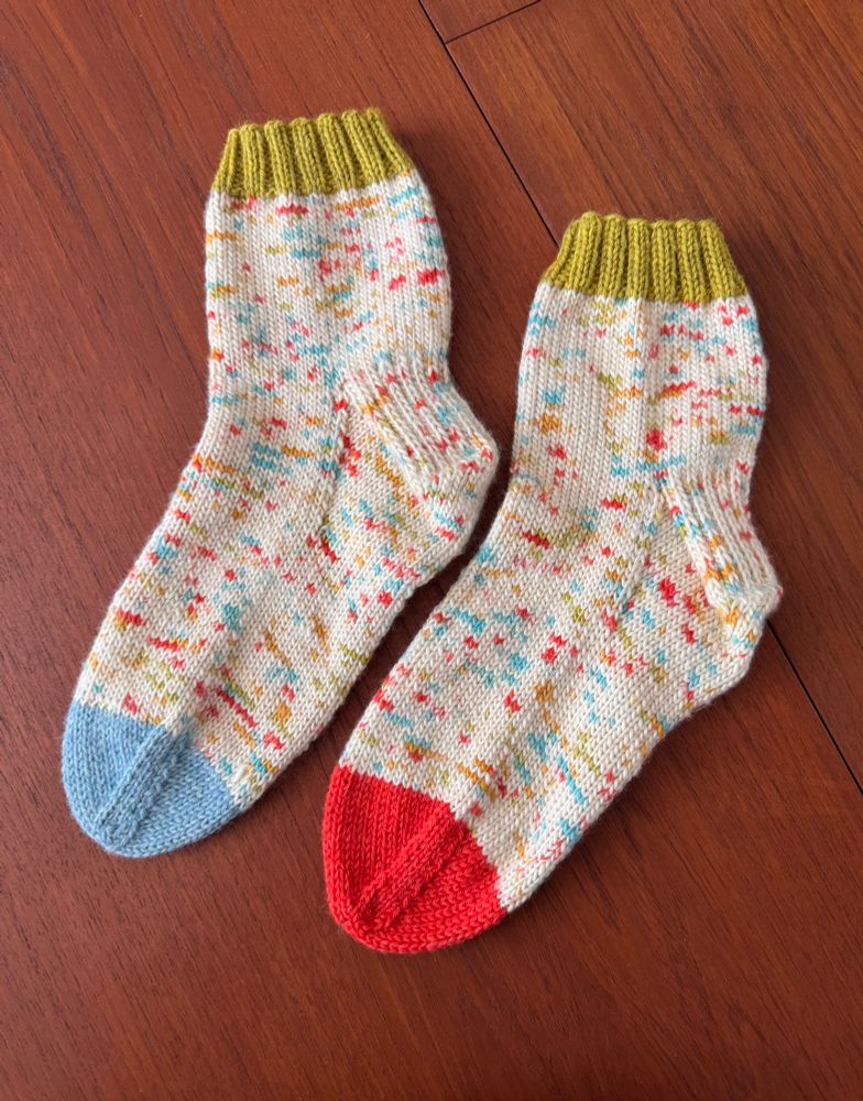 A pair of colorful hand knit socks resting flat on a wooden table