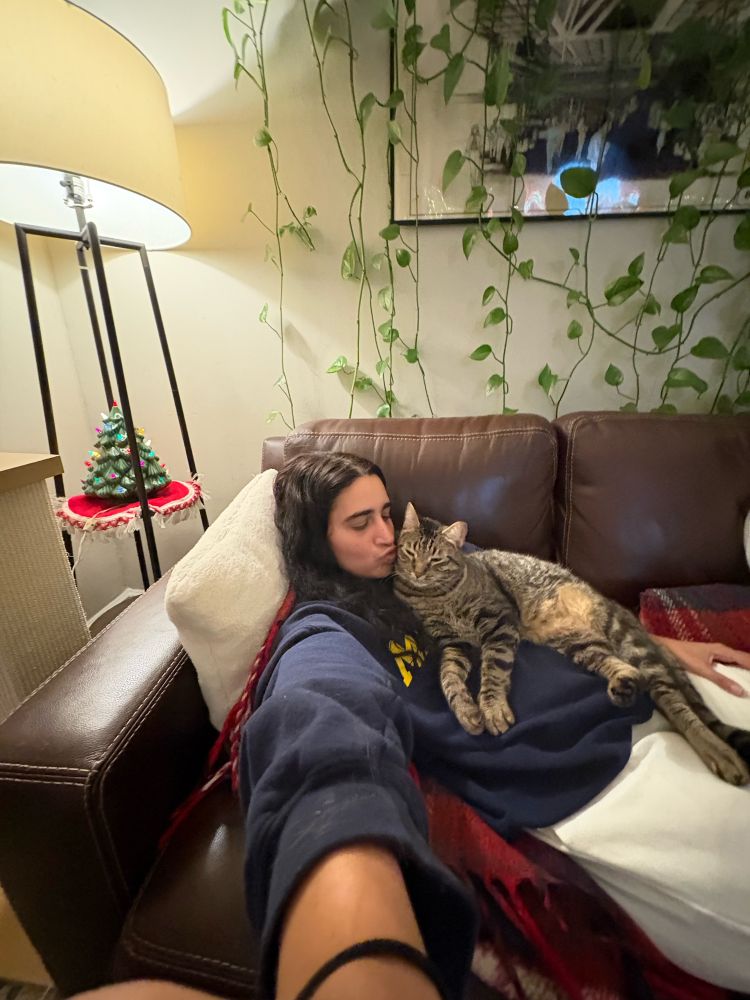 Kayla Kumari Upadhyaya on her couch with her cat Timmy Tomato