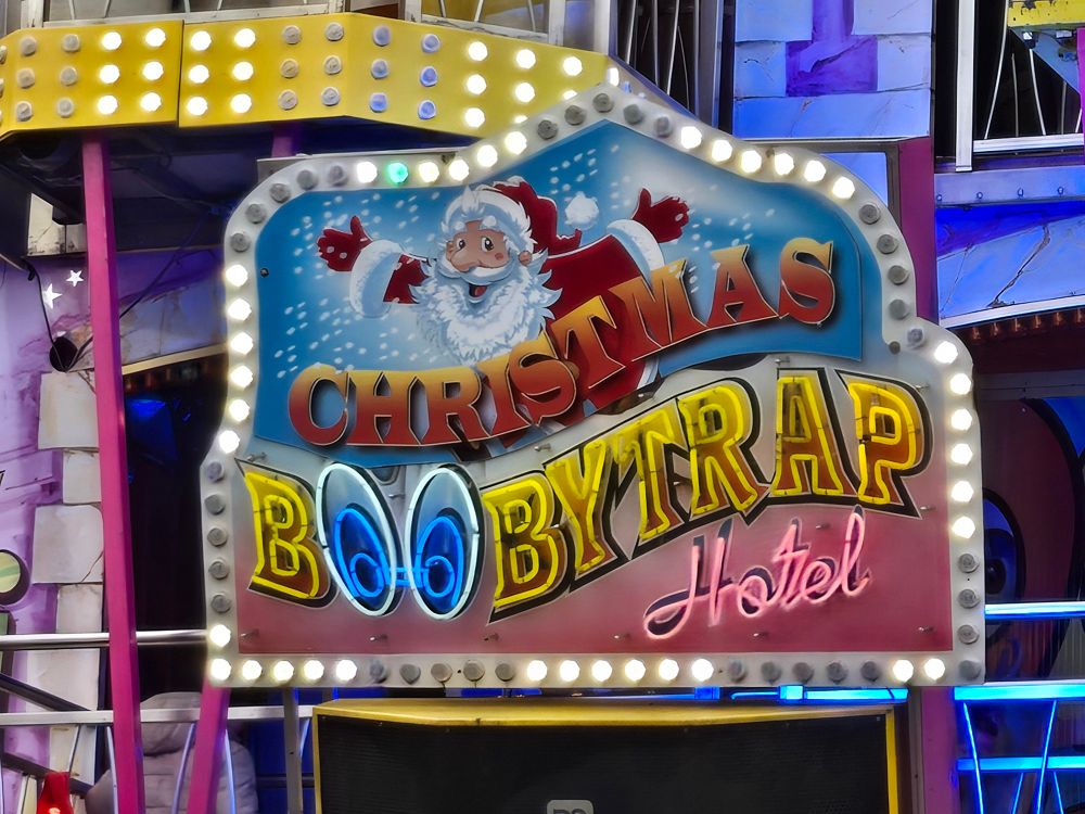 A lighted sign for a carnival fun house reads "christmas boobytrap hotel"