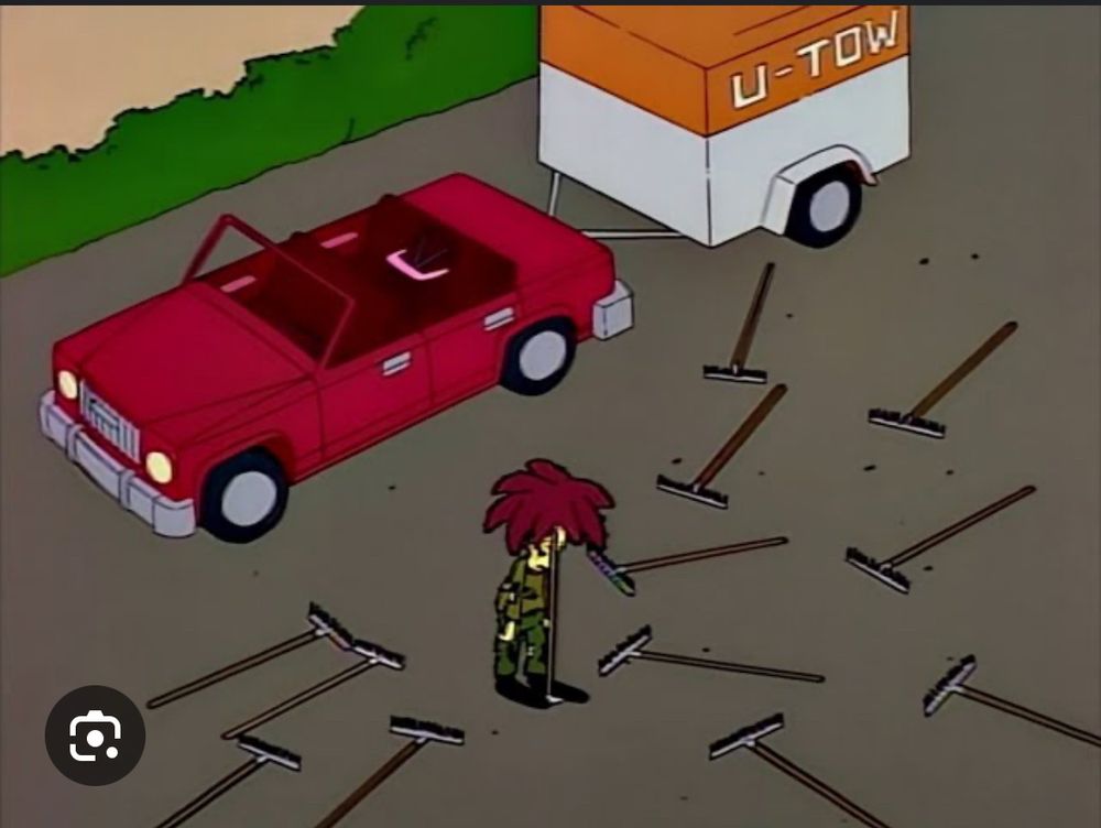 Sideshow Bob stands in front of a car pulling a trailer, surrounded by rakes.