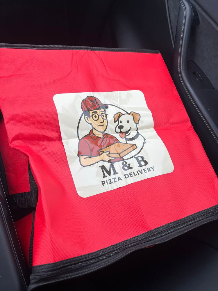 A picture of a pizza box with a cartoon man in a red shirt and red hat, and a puppy dog. The words say “M&B Pizza Delivery.”