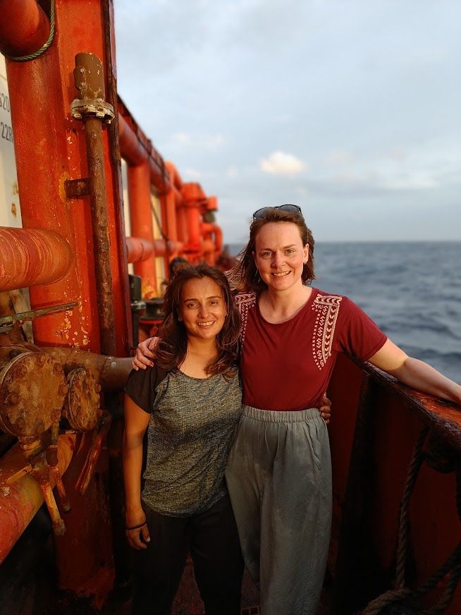 Rucha and Ruth on the research vessel after a day of SCUBA diving and carrying SCUBA tanks backwards and forwards (hence some damp patches on their clothes)