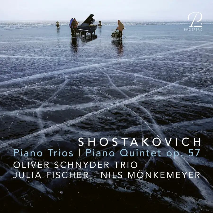 On this striking album cover, musicians stand on a vast, frozen lake, performing on a grand piano set directly on the ice. The cracked, translucent surface adds a haunting beauty, echoing the emotional intensity of Shostakovich’s music. Above, the sky merges with the horizon in a bluish haze, evoking isolation and resilience. The album features Shostakovich's *Piano Trios* and *Piano Quintet op. 57*, performed by the Oliver Schnyder Trio, violinist Julia Fischer, and violist Nils Mönkemeyer, released by Prospero. A poetic, icy visual for one of the 20th century’s most introspective composers.
