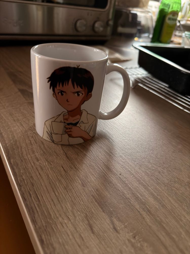 A mug with Shinji Ikari from Evangelion on it also holding a mug and looking annoyed 