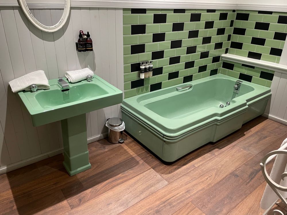 A view of the bathroom sink and bathtub which are both green and possibly 1920s or 1930s in appearance