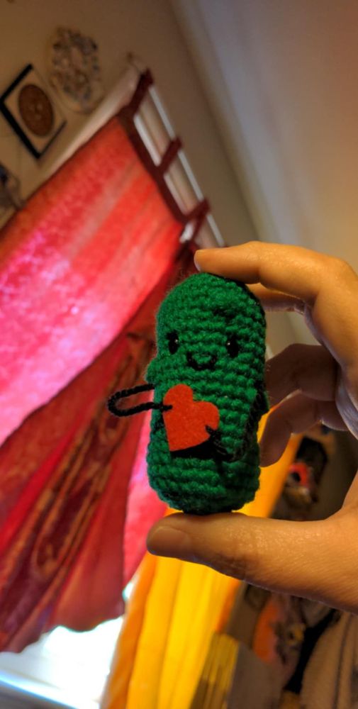 Photo of a crochet pickle with string arms holding a red felt heart