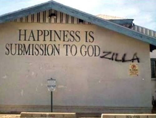 Vandalized inscription on the side of a building that reads 

HAPPINESS IS
SUBMISSION TO GODZILLA