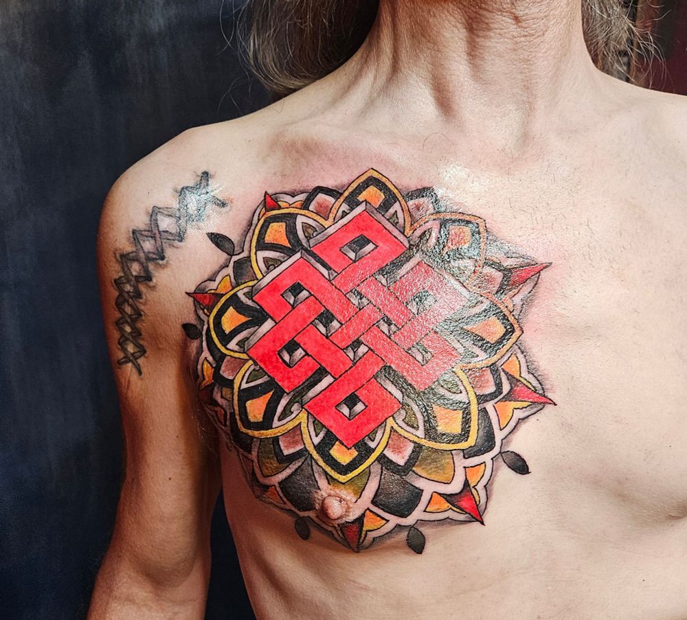 A large, colorful mandala right side chest tattoo with a large red buddhist knot in the center