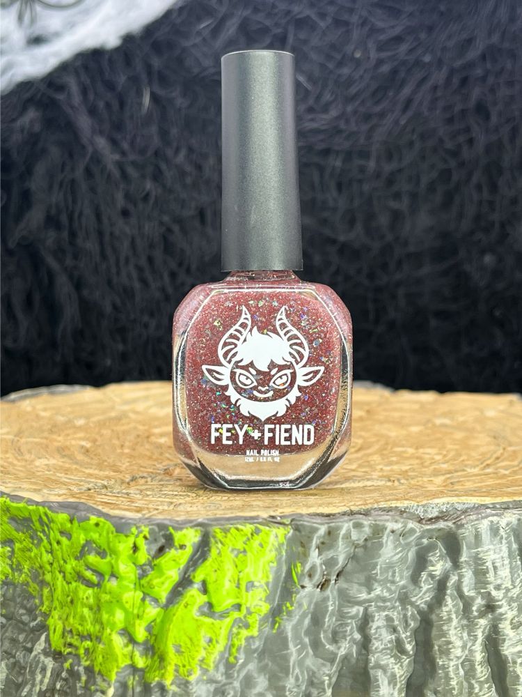 Product shot of nail polish bottle on a mossy stump platform: Ruby red glitter and silver holo shreds with glow-in-the-dark pigment