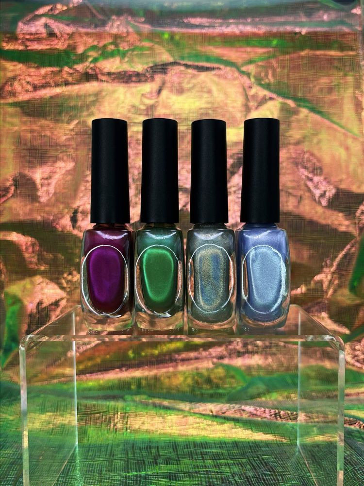 Product shot of the sides of four nail polishes from Fey+Fiend’s Gay Ass Summer Set from left to right:

Diva Up (deep magenta), Feelin’ Feral (shimmery forest green), Good Boy (silvery-lavender with violet sparkles), and Gay Sh*t (holographic glitter in clear top coat)