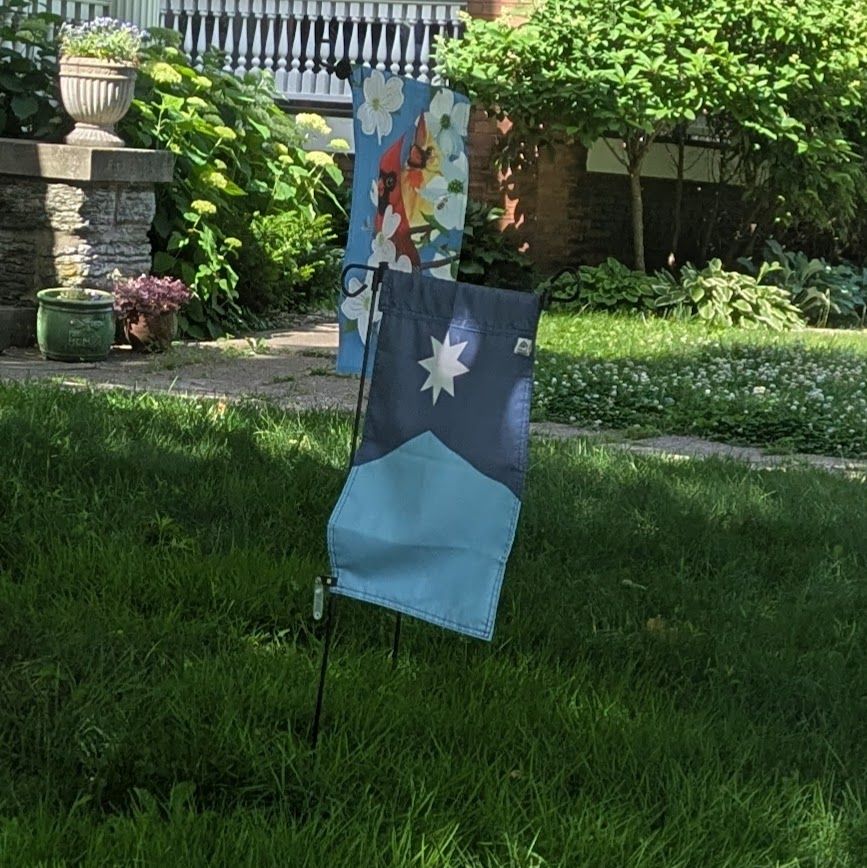 A Minnesota state garden-size flag in a front yard in Saint Paul, MN, behind it is a garden-sized flag with two cardinals and tulips.