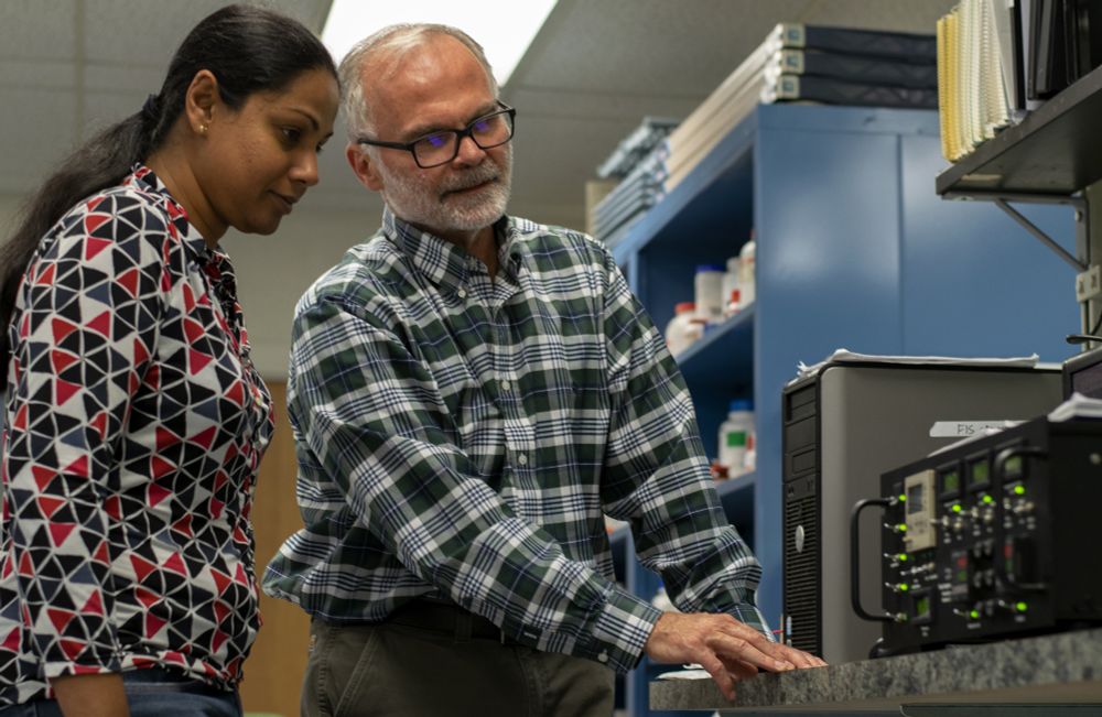 Tom Sharkey and former lab member, Sarathi Weraduwage, examine a piece of equipment.
