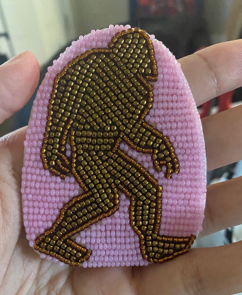 an archway shaped piece of beadwork. there is a silhouette of bigfoot in the center of the piece. the silhouette is beaded in metallic brown beads. the background of the piece is bubblegum pink. the beadwork is being held in hand. 