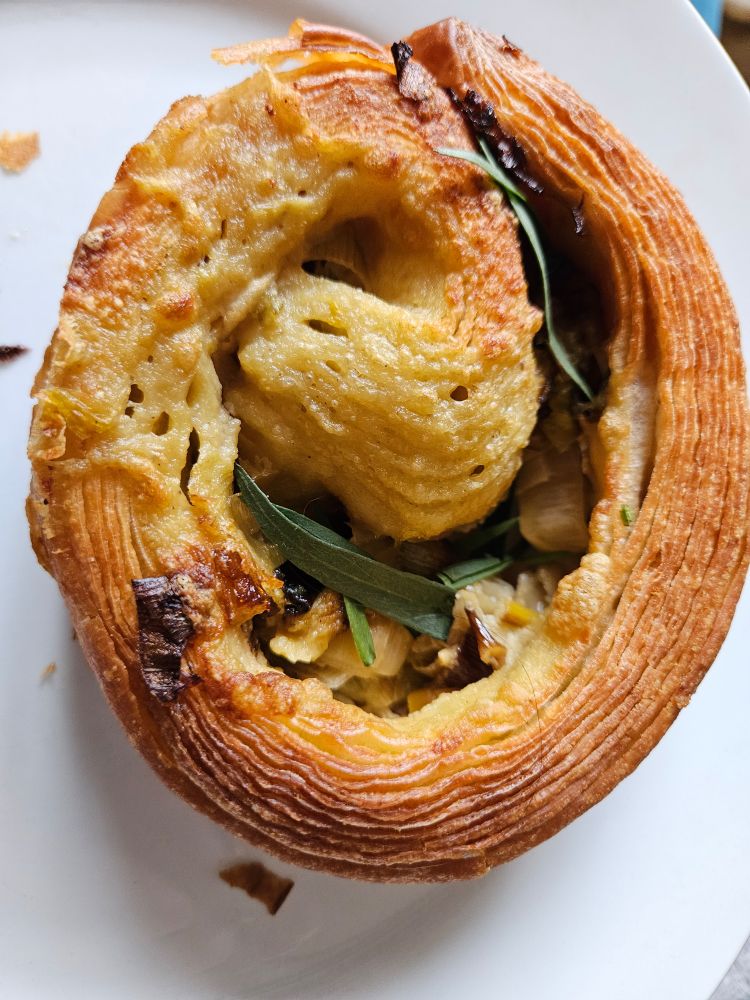 Photo of a flakey swirl shaped pastry. The filling of cheese, leeks, and herbs are visible. The pastry is vegan, but you'd never be able to tell the difference.