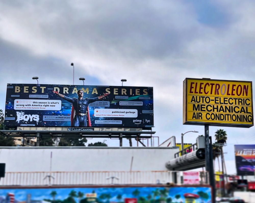 Against a cloudy sky in Studio City, CA, a billboard promoting The Boys as “Best Drama Series” features Homelander with his arms spread wide, almost as if he’s embracing the flurry of one-star pans and critiques of our most recent season. To the right of the Boys billboard is a yellow sign for Electroleon, an auto shop.
