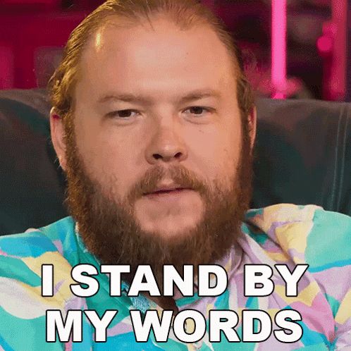 a man with a beard is sitting on a couch and says " i stand by my words "