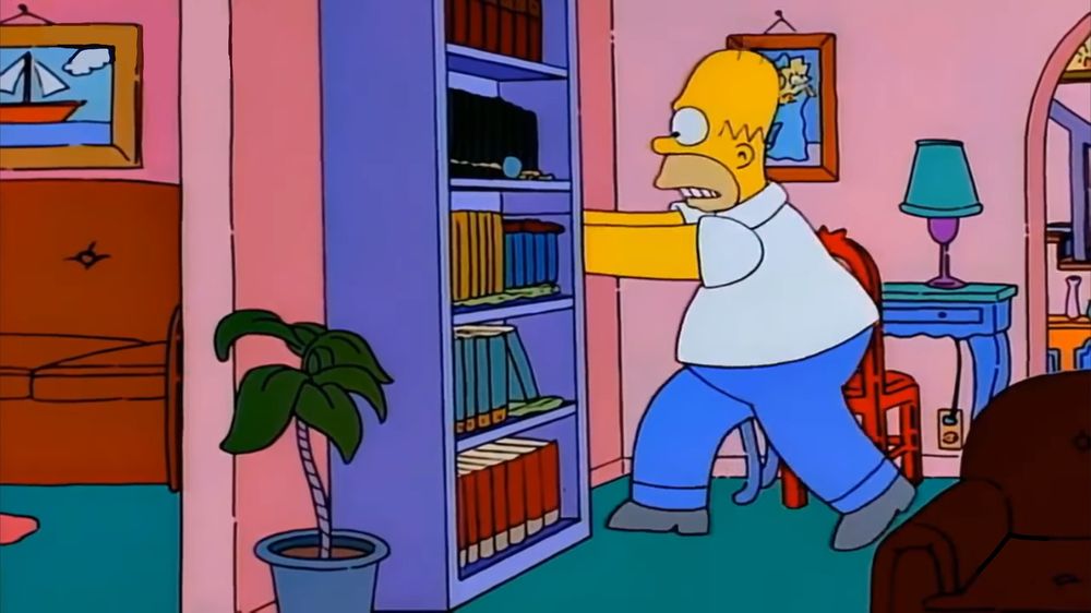 A still from ‘The Simpsons’ of Homer running to hide behind a bookcase