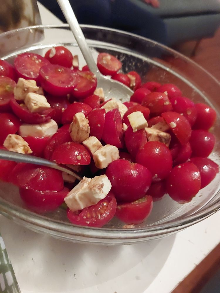 Un petit saladier en verre avec des tomates cerises coupées et de la fêta. 