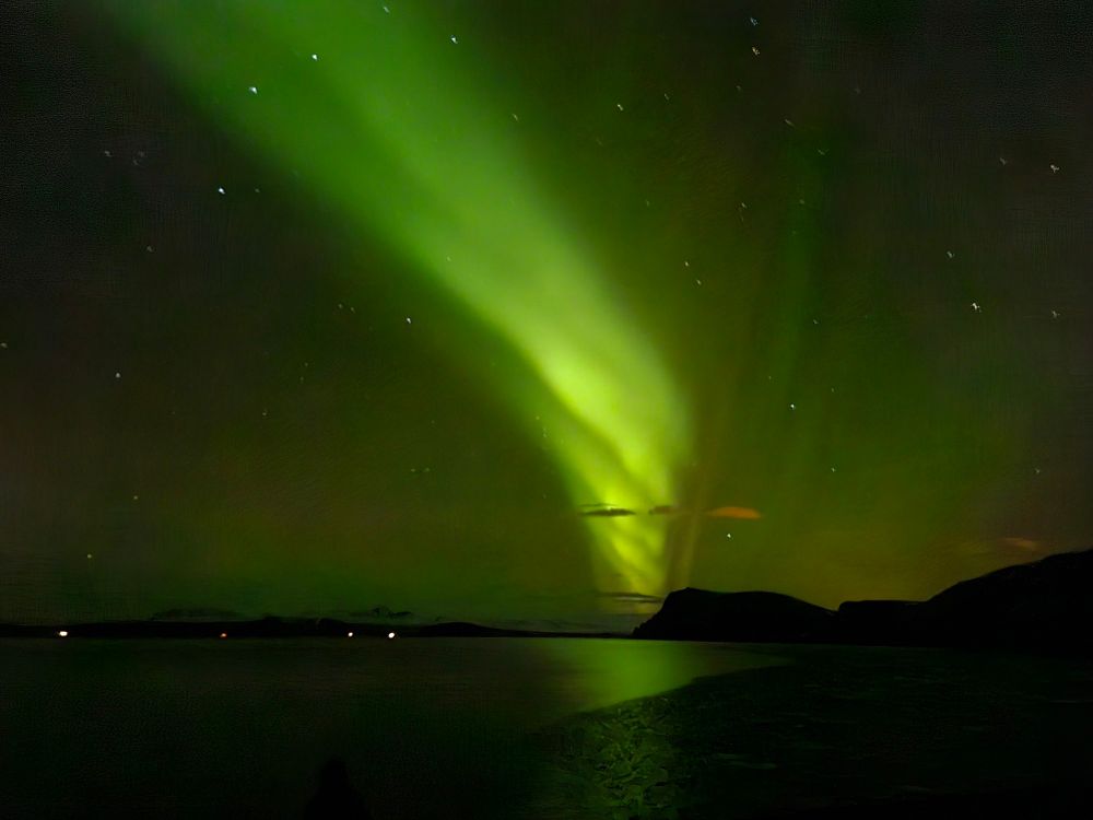 a green streak of aurora across the night sky, a lake in the foreground 