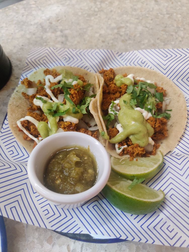 Two soft shell tacos and two lime slices on a plate, with a small dish of salsa beside them.