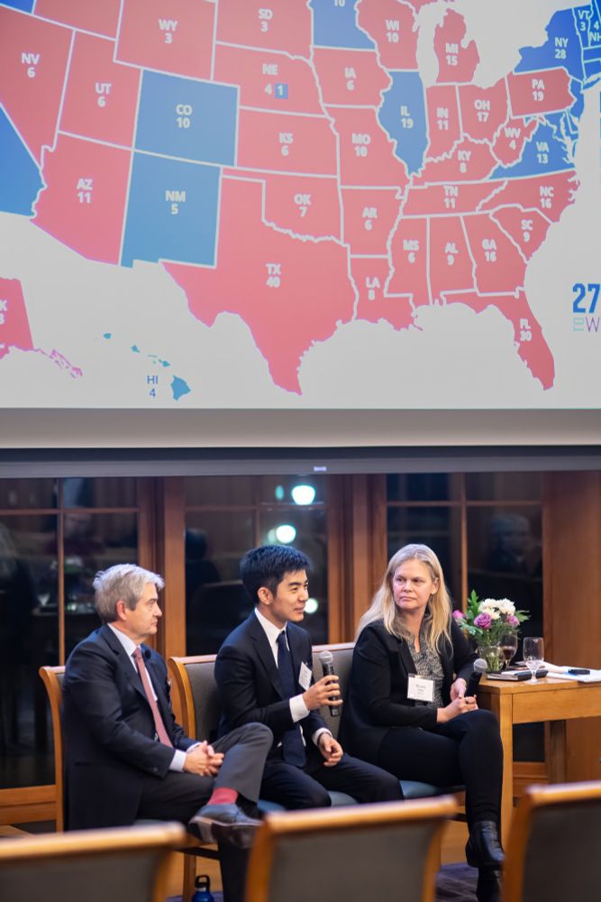 Shiro Kuriwaki speaks in a conference room, next to Stephen Ansolabehere and Beverly Gage, seated in front of a projection screen showing a red-blue U.S. election map.