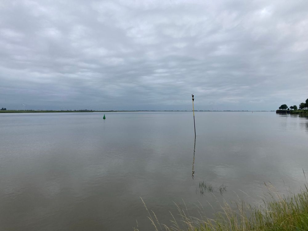 Ruhiger Fluss, darüber grauer Wolkenhimmel, der sich im Fluss spiegelt.