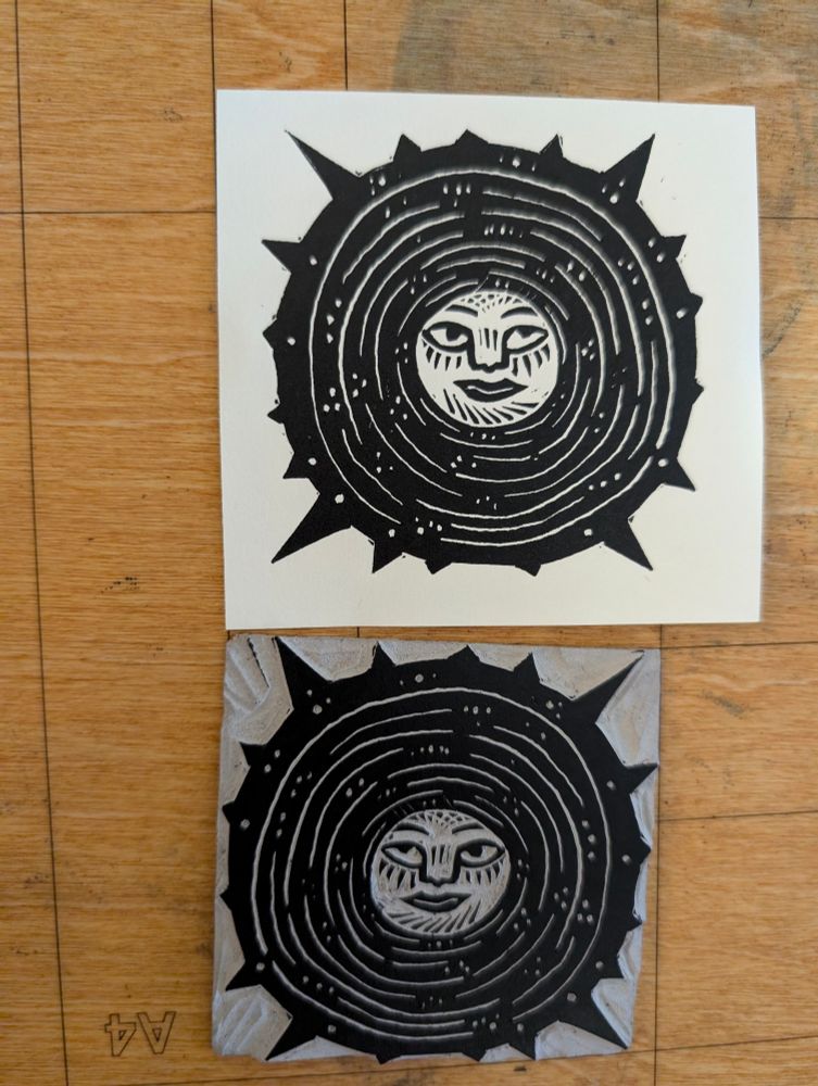 Linocut of a black sun with a head in the middle. Er can see the block and the print above.