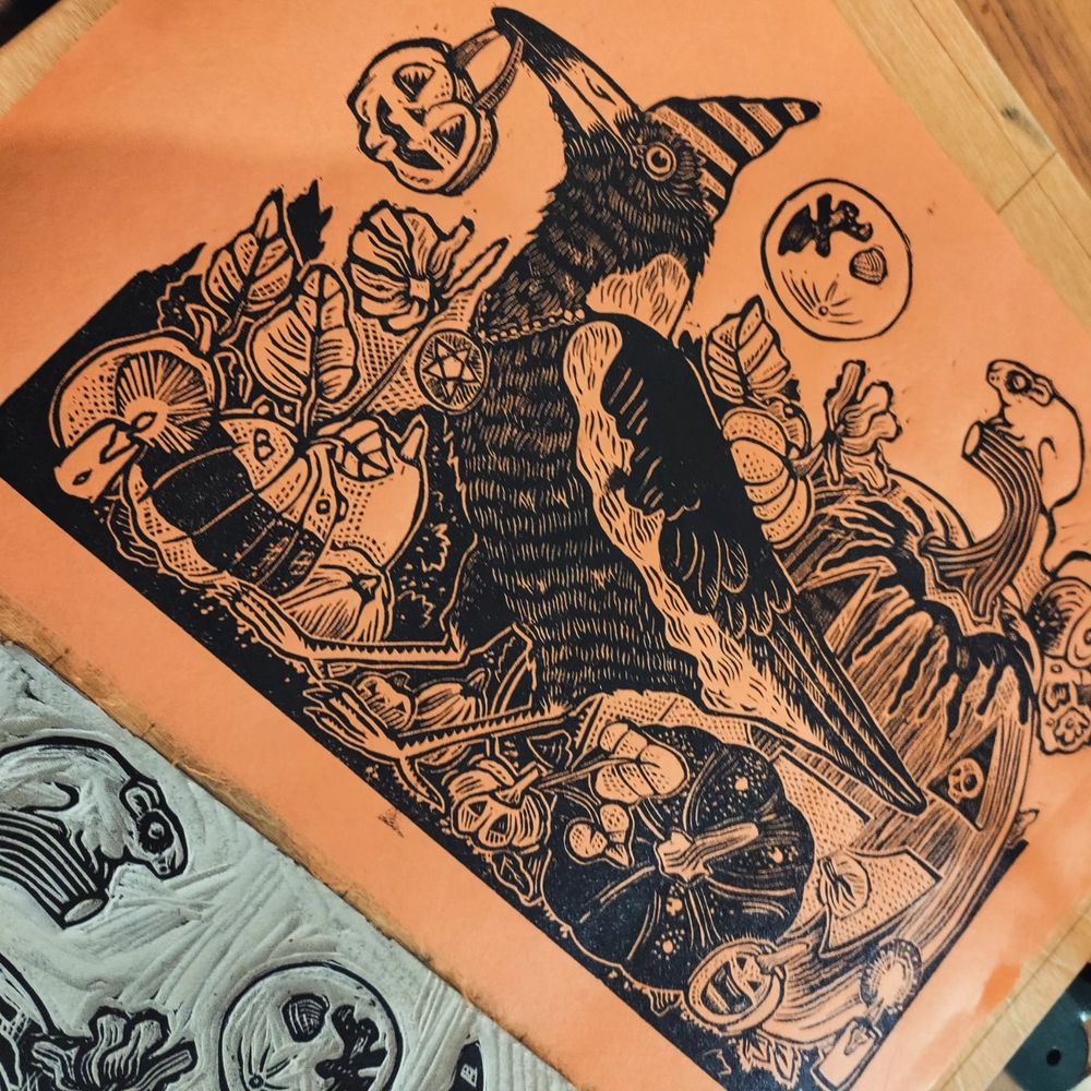 Linogravure imprimée sur papier orange. Corbeau avec une citrouille dans le bec, entouré de citrouilles d'Halloween 