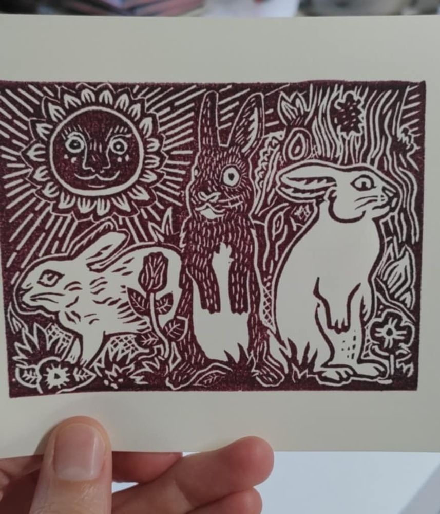 Impression bordeaux sur papier crème. Trois lapins deux blanc et un noir. Deux sont debout. On voit le soleil avec un visage à l'arrière plan 
