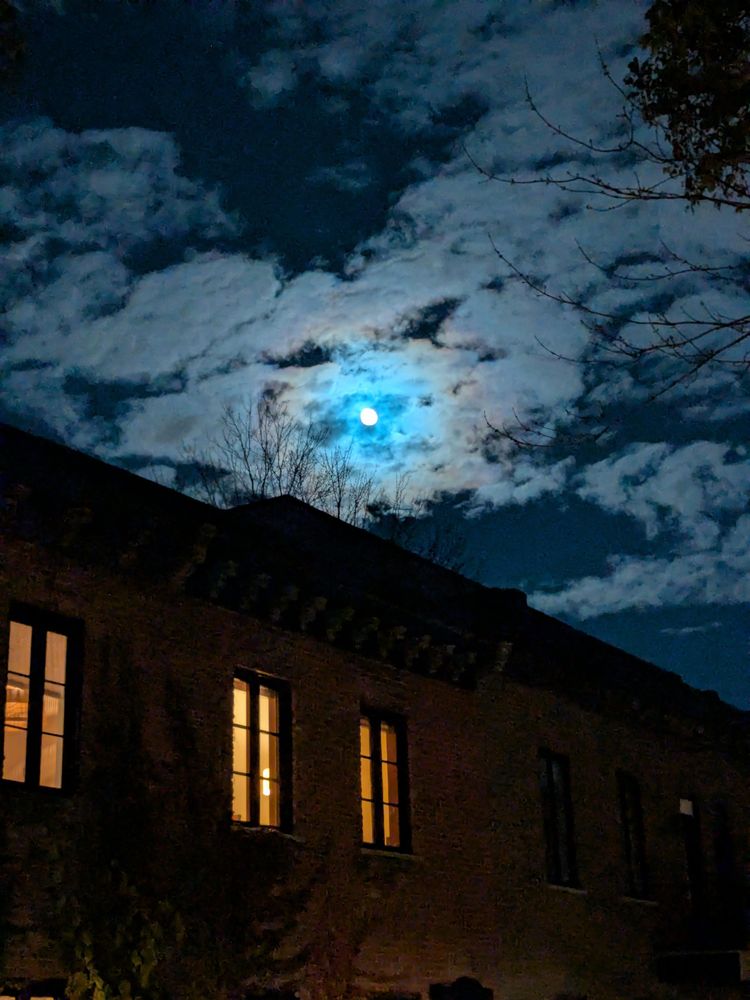 A almost full moon behind clouds with a weird ring of turquoise and yellow around it