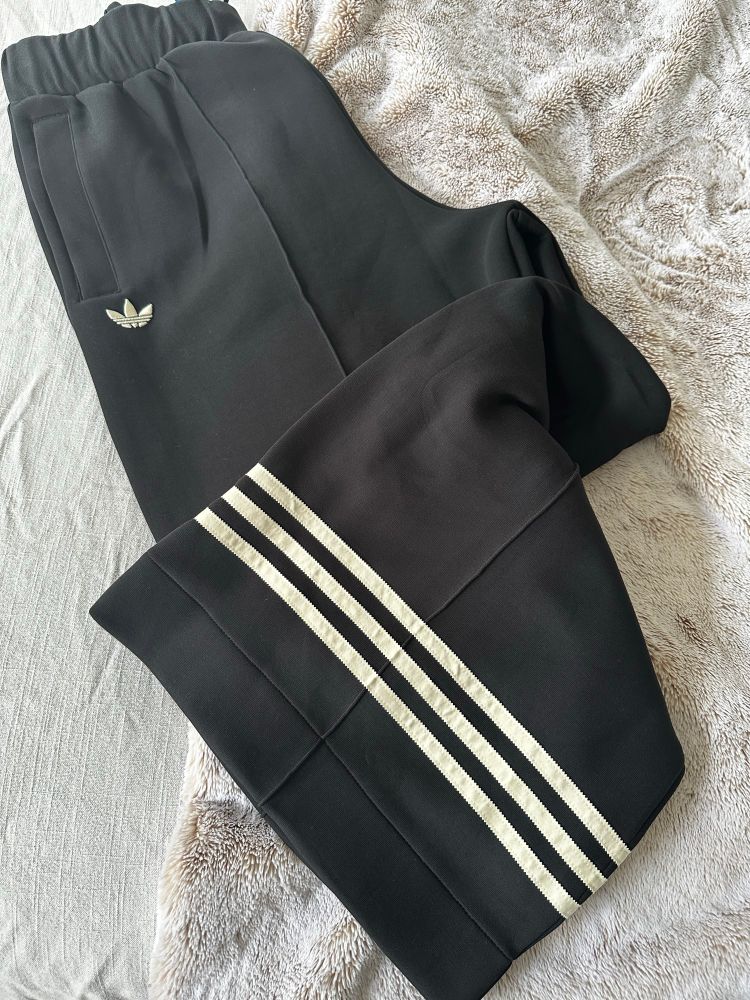 Black wide leg Adidas track pants on light gray fur blanket. 