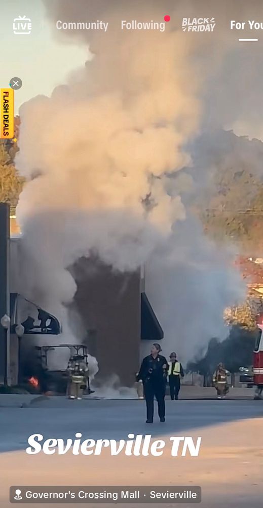 A screenshot from TikTok that says Sevierville Tennessee. It shows rescue workers at the scene of a strip mall where a truck plowed into a store and promptly caught fire and exploded, but there is also in the upper left corner A small TikTok store promo that says flash deals in all caps
