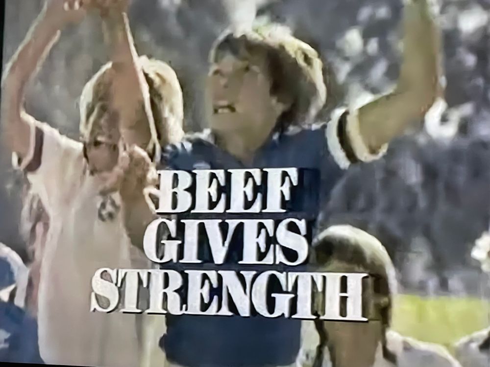 A beef council ad from the 1970s featuring several young white men with their arms raised in victory and the all caps text on the screen reads BEEF GIVES STRENGTH