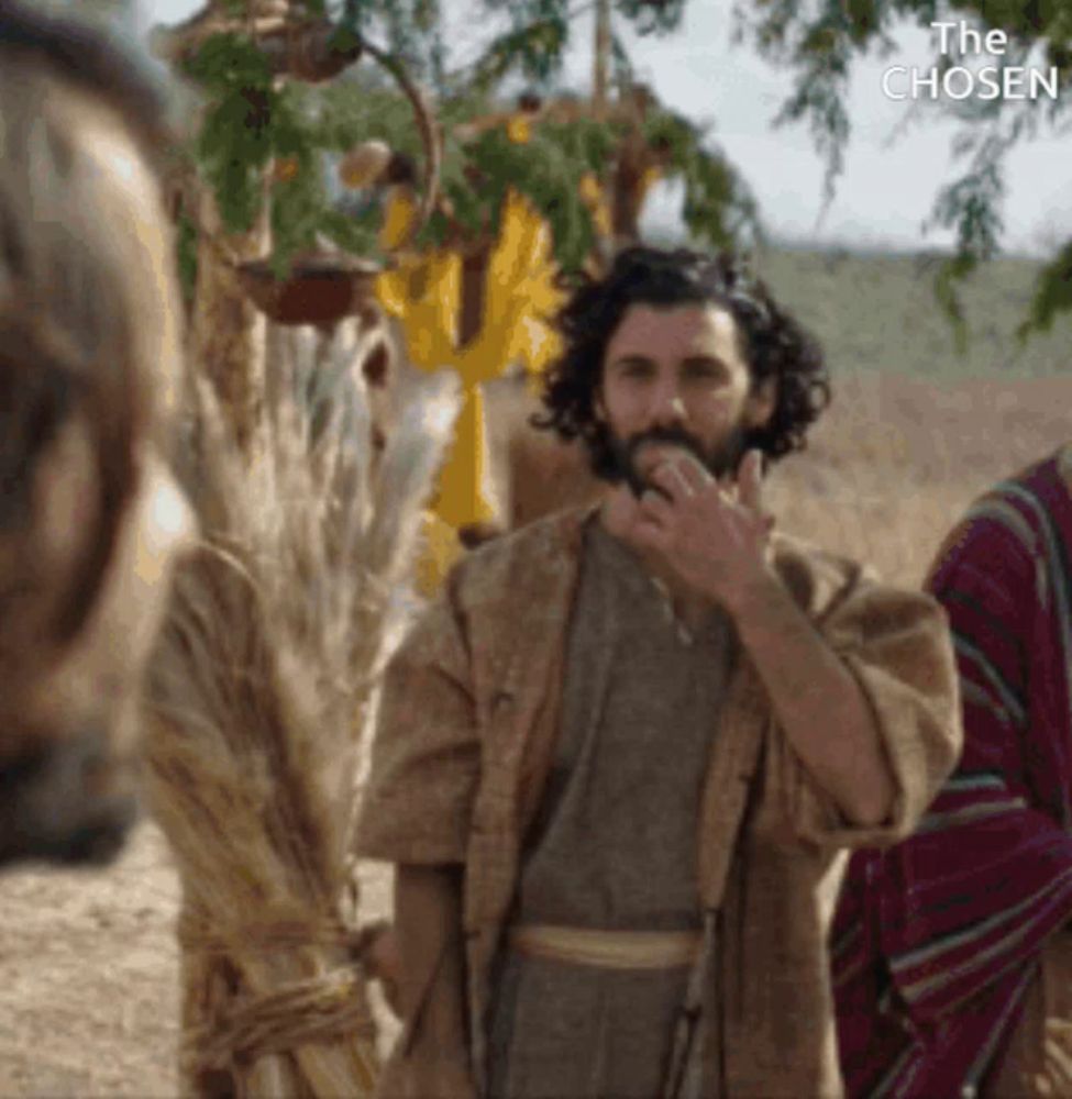 a man with a beard is standing in a field with a bunch of wheat in his hand .