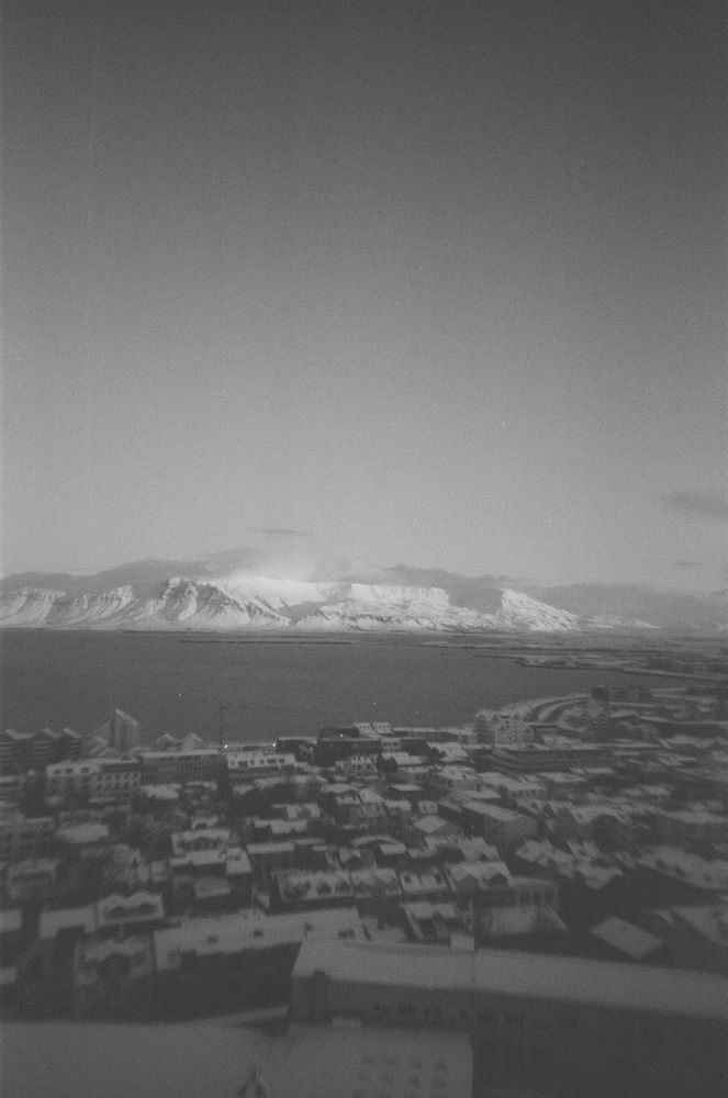 A view across Reykjavik from Hallgrimskirkja's tower. Mostly everything is grey but there's an interesting bright white light reflecting off the top of the Esja volcano range on the other side of the bay.