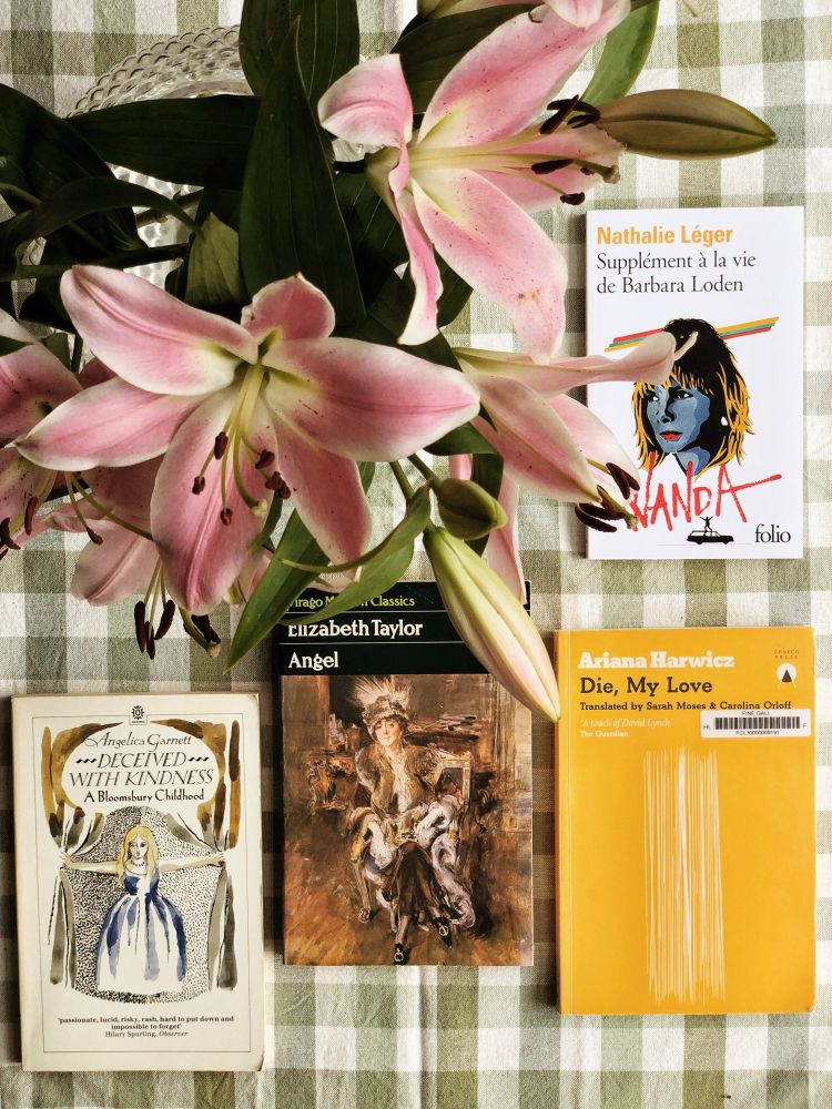 4 books and a vase of pink lilies on a green gingham tablecloth. The 4 books are Deceived with Kindness by Angelica Garnett, Angel by Elizabeth Taylor, Die, My Love by Ariana Harwicz and Supplément à la vie de Barbara Loden by Nathalie Léger