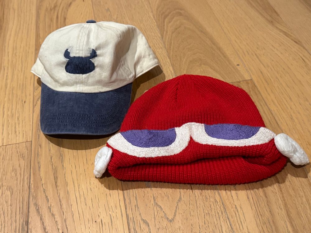 A baseball cap with a beetle insignia alongside a red Puyo hat.