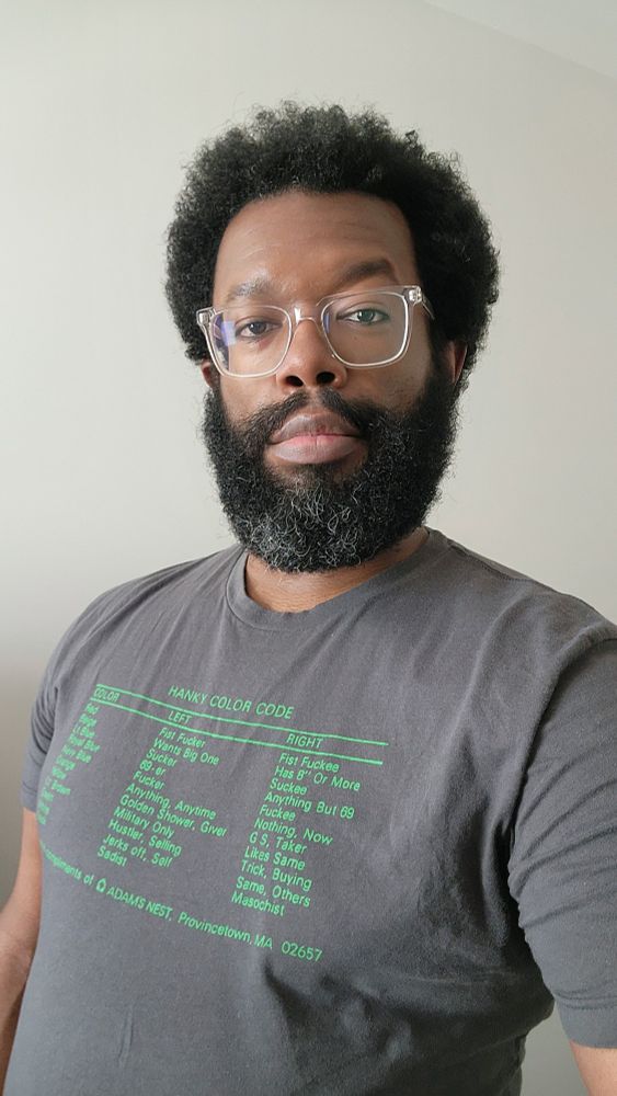 Self-portrait of me making eye contact with the camera with a subtle smile/grin on my face. My tee shirt has a condensed version of the hanky code printed on the front.