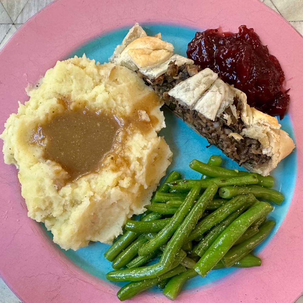 Thanksgiving dinner plate with a slice of Mushroom Wellington, cranberry sauce, mashed potatoes with gravy, and green beans.