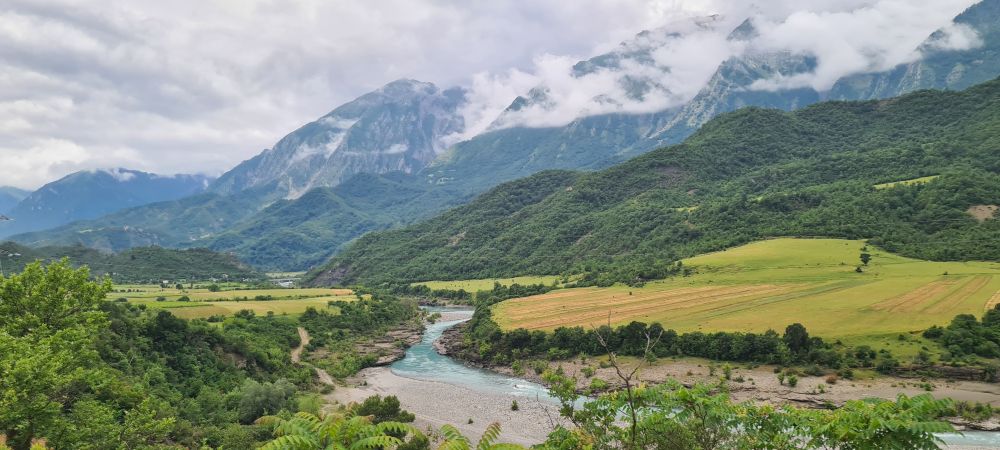 photo de paysage de fond de vallée avec une rivière bleue qui passe au milieu de champs entourés de montagnes. y'a trop de nuages