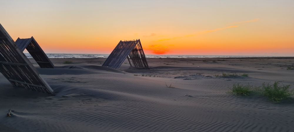 une plage de sable au soleil couchant, avec des abris en bois genre cabanes mais avec juste un toit écoutez je suis nul pour décrire désolé