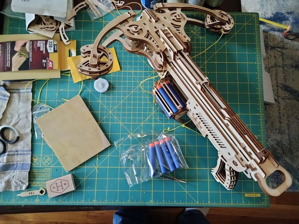 A wooden crossbow on a crafting mat. The crossbow has an open cylinder and holds 6 nerf darts.